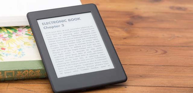 Leitor de livros eletrónicos numa mesa de madeira, ao lado de um livro impresso